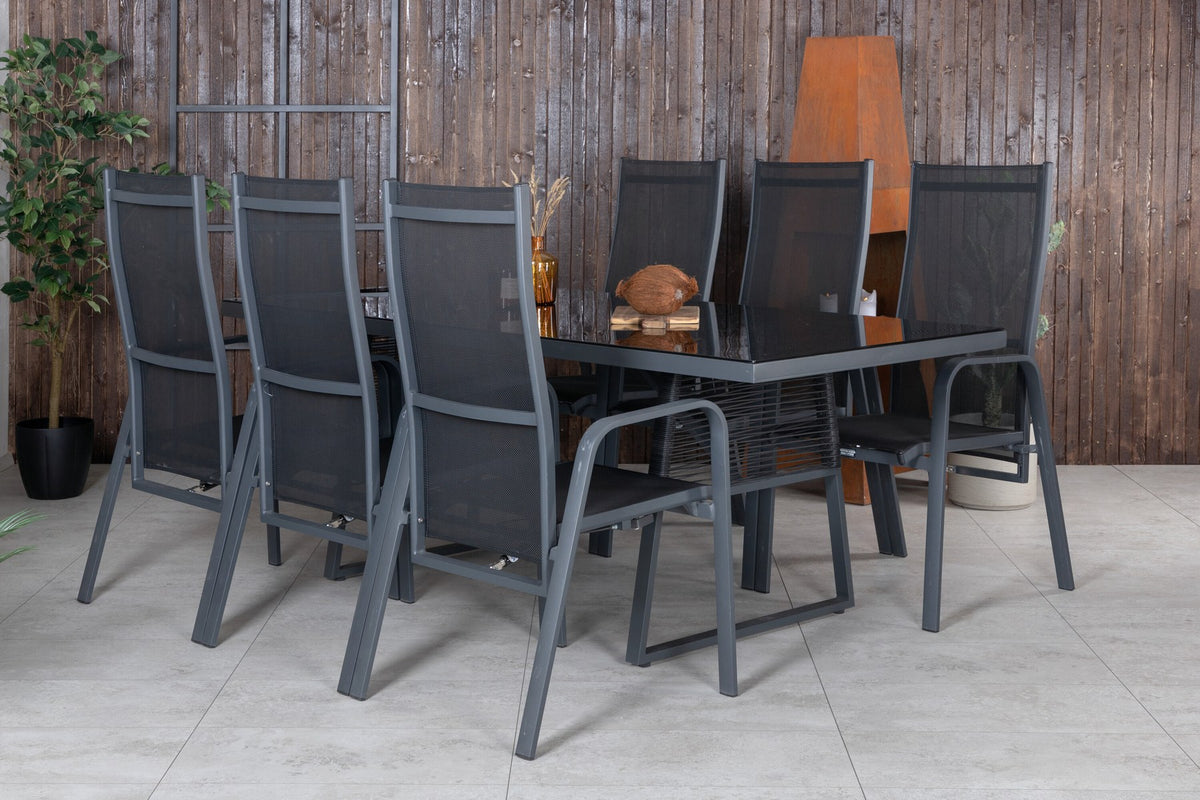 Foto eines rechteckigen Esstisches aus schwarzem Glas mit Aluminiumbeinen und zwei schwarzen Relaxsesseln aus Geflecht im Freien.