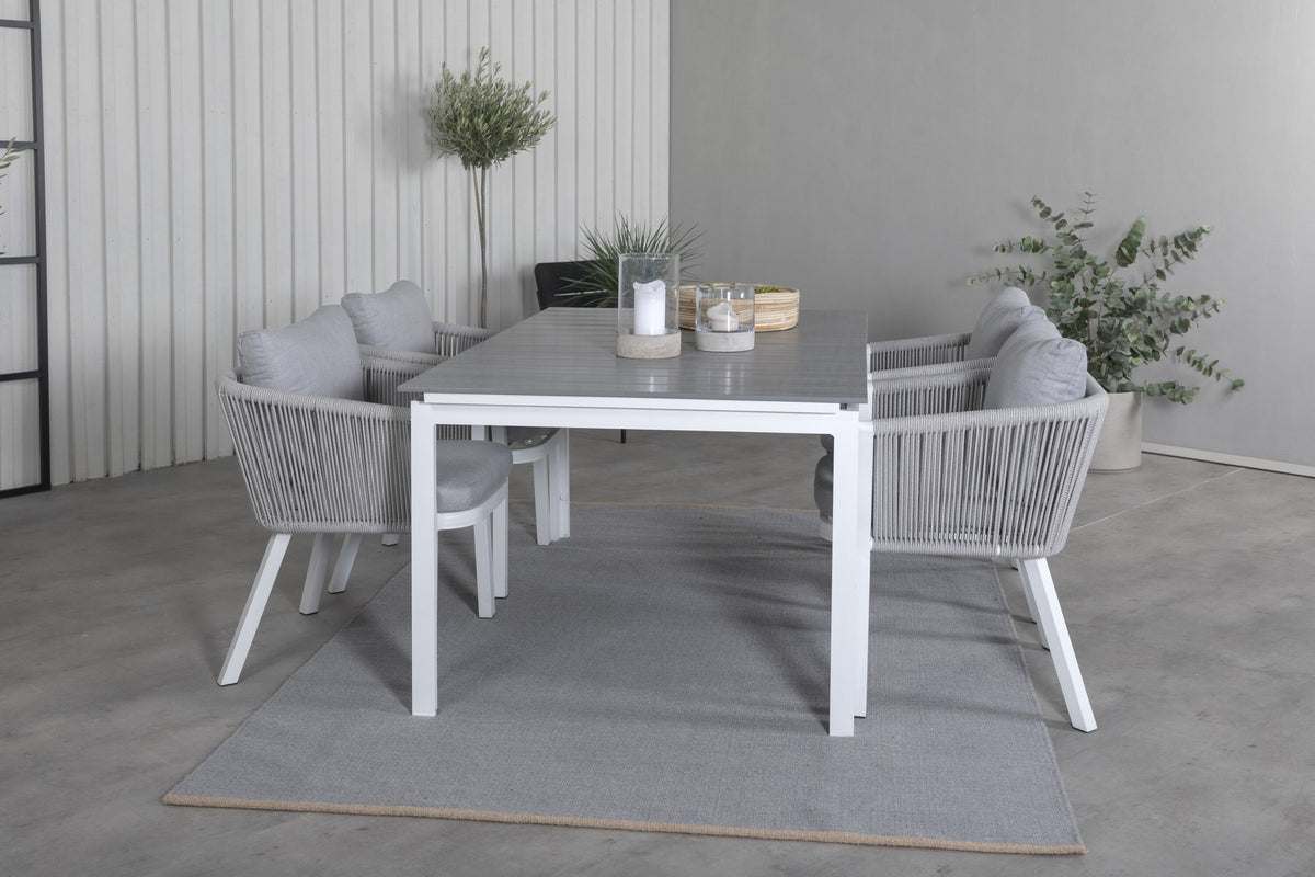 Zwei graue Esszimmerstühle mit Seil-Bezug und Aluminiumgestell neben einem weissen, ausziehbaren Aintwood-Esstisch im Garten.