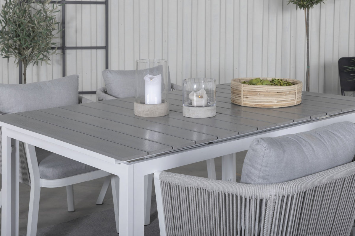 Zwei graue Esszimmerstühle mit Seil-Bezug und Aluminiumgestell neben einem weissen, ausziehbaren Aintwood-Esstisch im Garten.