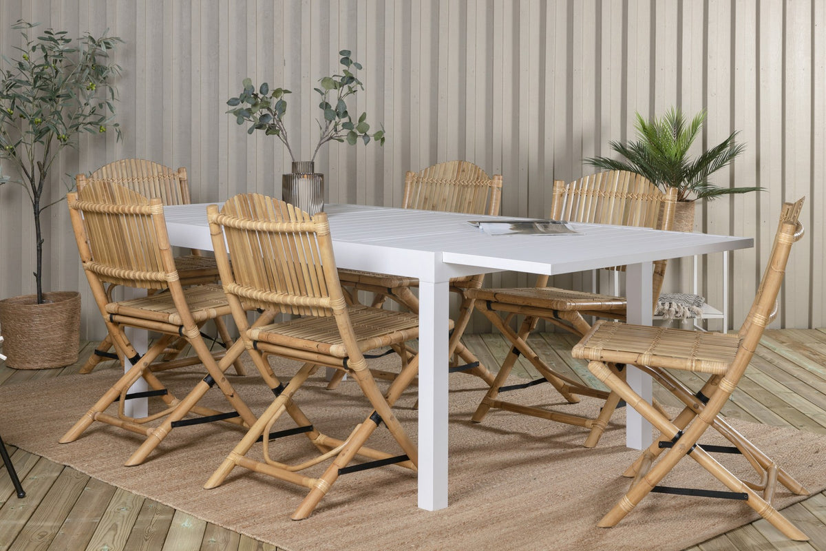 Aluminium-Caféstuhl in Natur mit Baumwoll-Polyester-Bezug neben rechteckigem Esstisch mit weisser Aluminium-Tischplatte und Rattanbeinen.