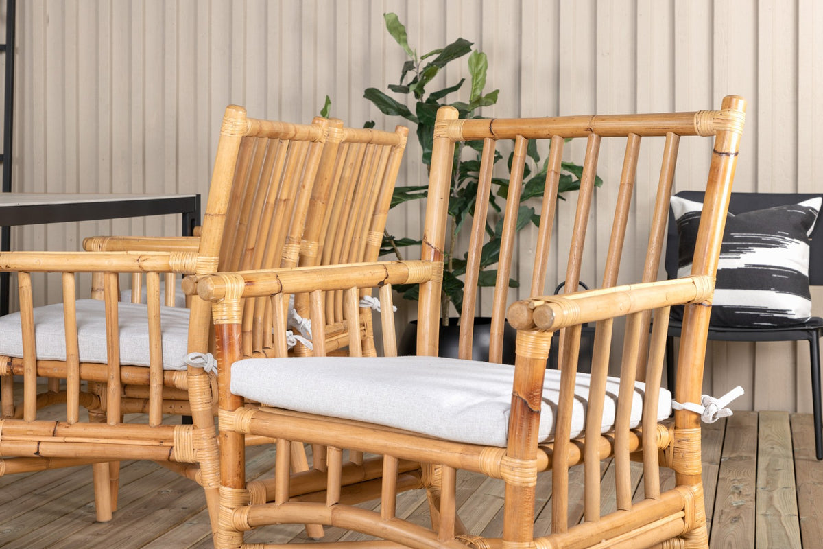 Rechteckiger Esstisch mit Glasplatte und Teakholzkante, schwarzem Metallgestell sowie Cane-Stühlen aus Rattan mit Bezug in Naturtönen.