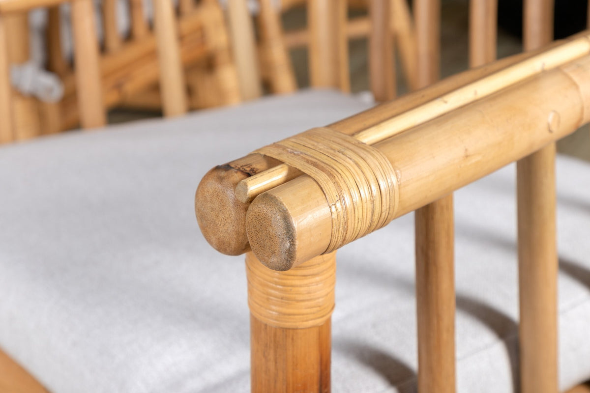 Rechteckiger Esstisch mit Glasplatte und Teakholzkante, schwarzem Metallgestell sowie Cane-Stühlen aus Rattan mit Bezug in Naturtönen.
