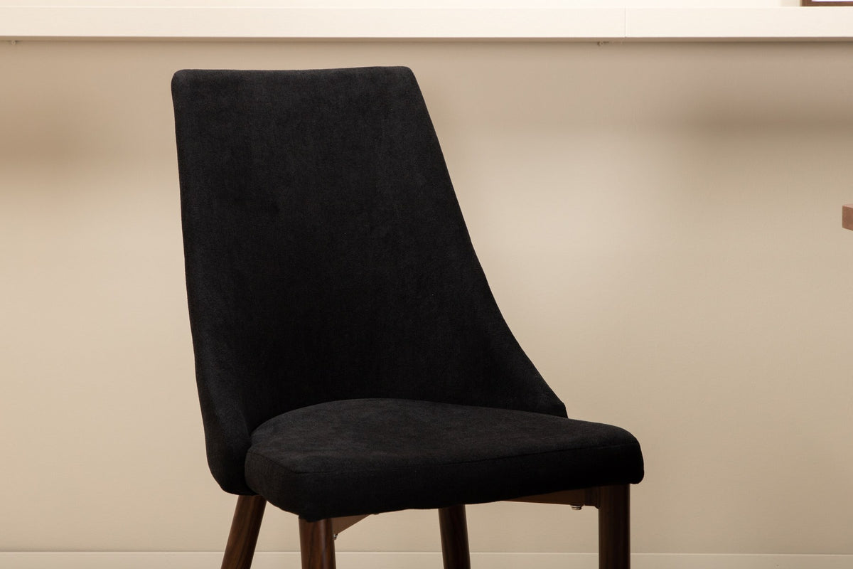 Rechteckiger Esstisch mit MDF-Tischplatte in Nussbaumfurnier und schwarzem Stahlgestell, kombiniert mit zwei schwarzen Polyester-Stühlen.