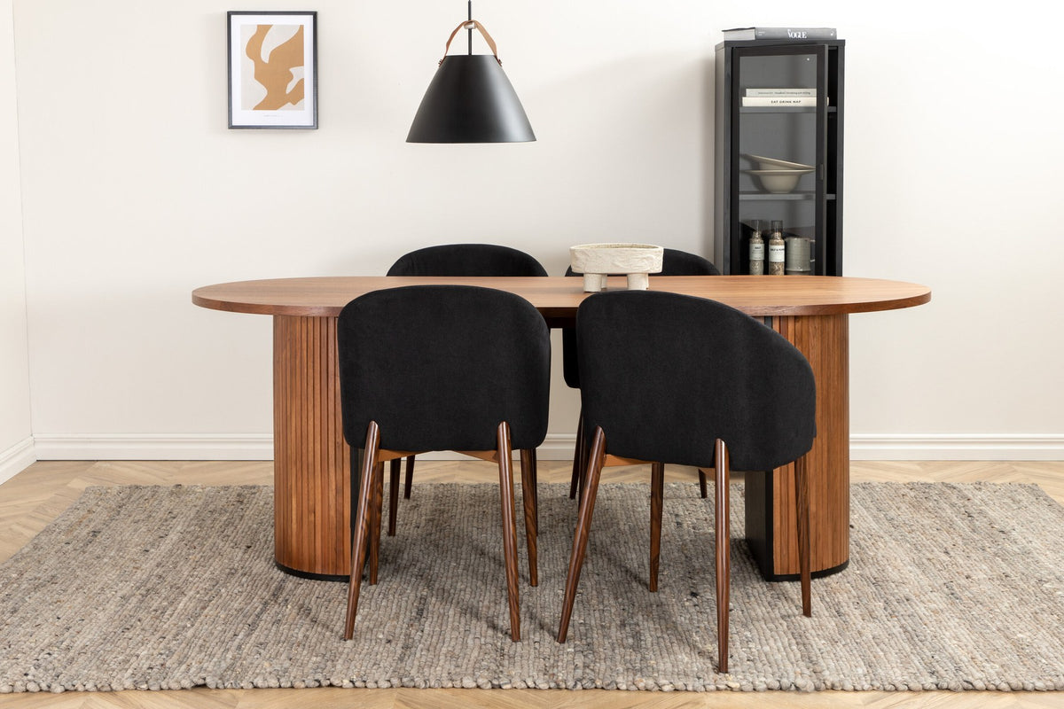 Ovaler Esstisch mit Nussbaum-MDF-Furnierplatte und Stahlgestell, daneben zwei schwarze Polsterstühle mit Metallbeinen im Esszimmer.