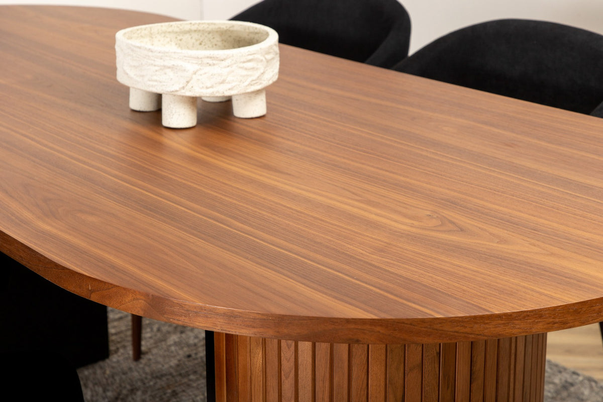 Ovaler Esstisch mit Nussbaum-MDF-Furnierplatte und Stahlgestell, daneben zwei schwarze Polsterstühle mit Metallbeinen im Esszimmer.