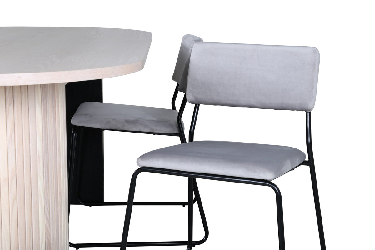 Zwei graue Esszimmerstühle mit schmalen schwarzen Beinen neben ovalem Esstisch mit MDF-Platte in Whitewash, Grösse 200x90 cm.