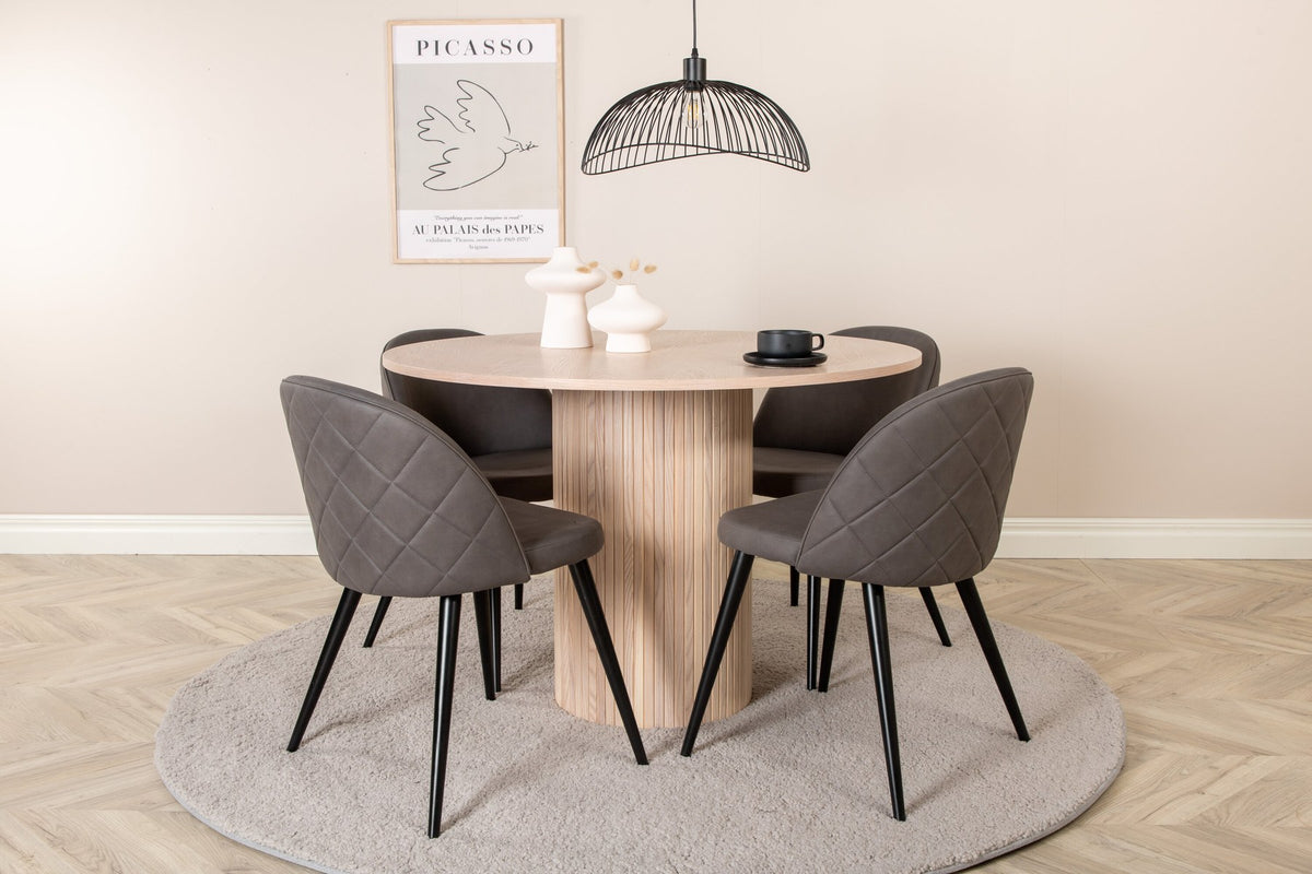 Runder Esstisch aus MDF in Whitewash mit ⌀110cm neben zwei Esszimmerstühlen mit grauem Mikrofaserstoff und schwarz pulverbeschichteten Eisenbeinen.
