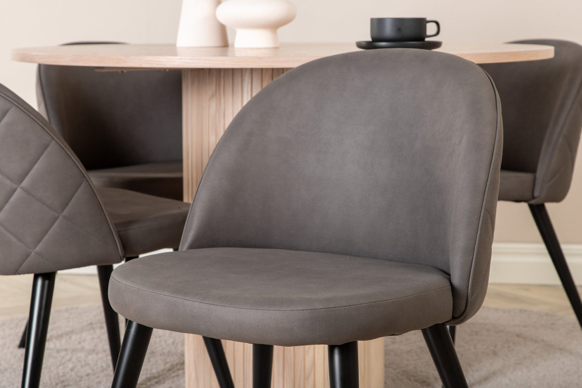 Runder Esstisch aus MDF in Whitewash mit ⌀110cm neben zwei Esszimmerstühlen mit grauem Mikrofaserstoff und schwarz pulverbeschichteten Eisenbeinen.