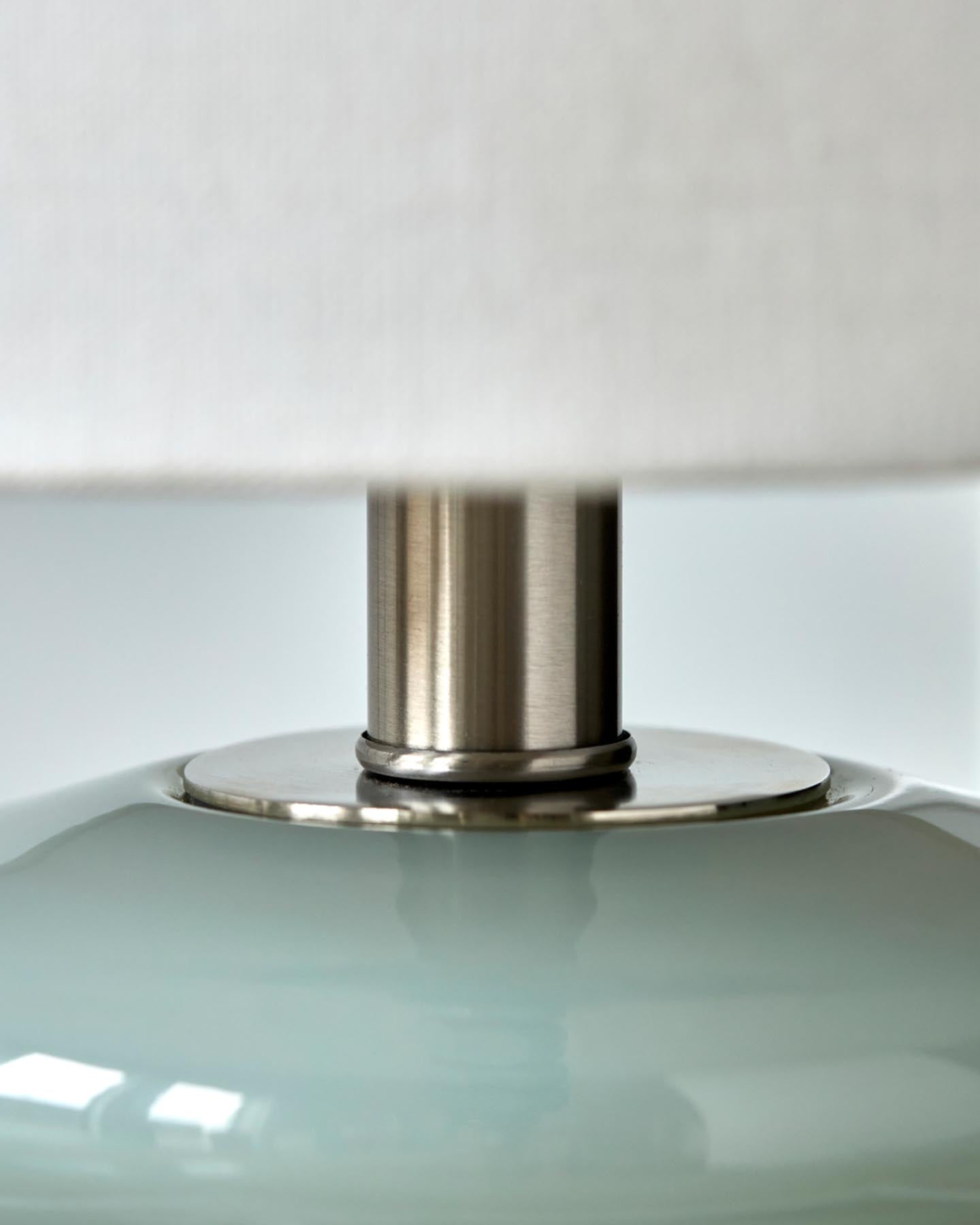 Entdecken Sie die stilvolle Tischleuchte HDStep S von House Doctor in Hellblau und Off-White. Handgefertigter Glasfuß und eleganter Baumwollschirm für ein gemütliches Ambiente.