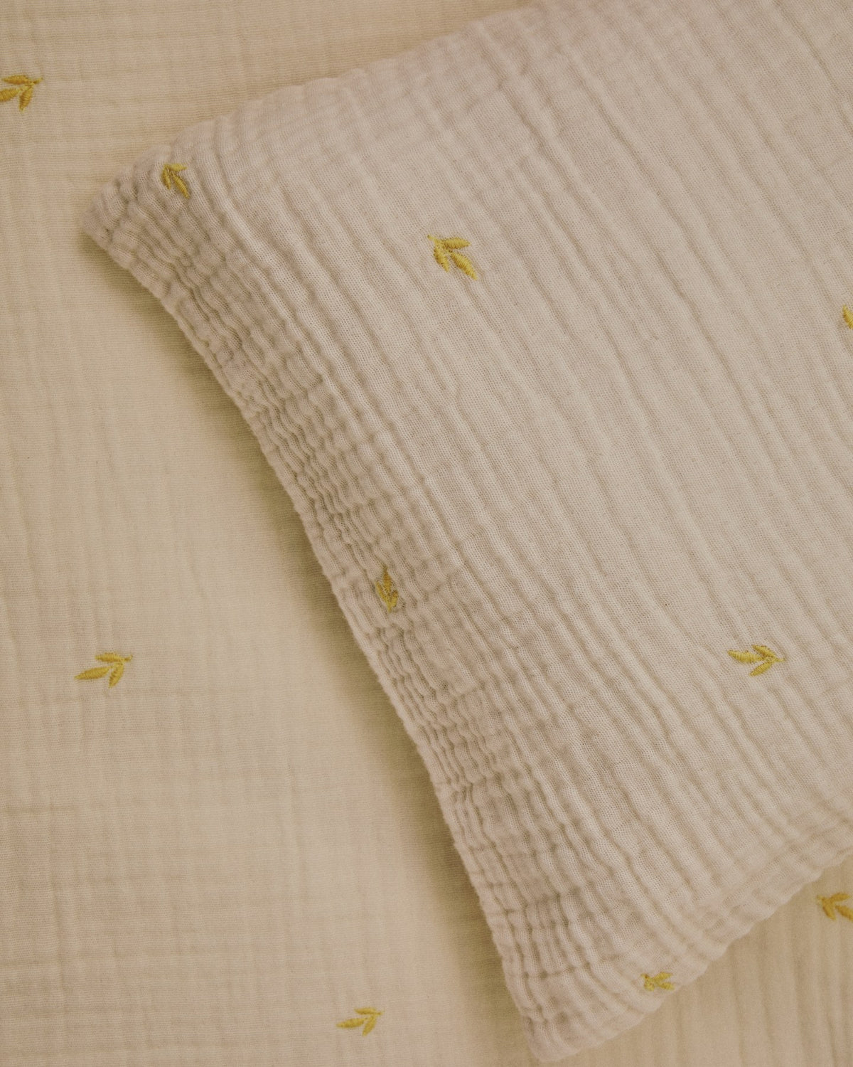 Bettbezug und Kopfkissen aus ecrufarbener Baumwoll-Doppelgaze mit aufgestickten Blättern, für Babybett, Set Dorani von Kave Home.