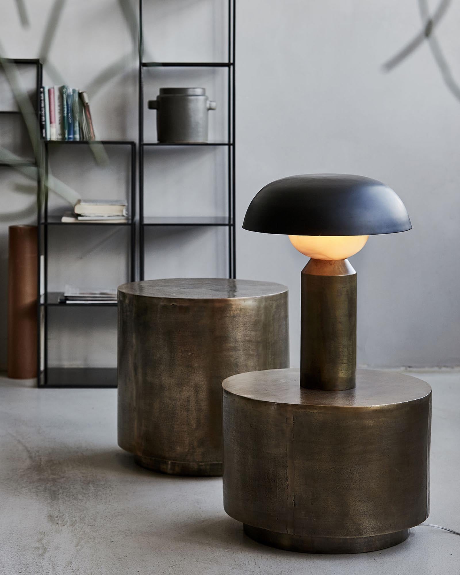 Die Big Fellow Tischleuchte von House Doctor kombiniert klassisches Design mit skulpturaler Eleganz. Aus Eisen und Glas gefertigt, bietet der schwarze Schirm einen stilvollen Kontrast zum goldenen Fuss. Perfekt für Sideboards.