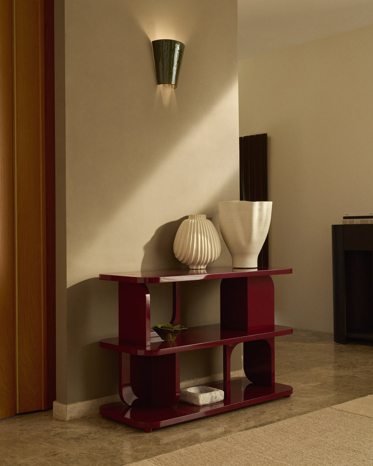 Regal Aduma aus MDF und Buchenholz mit granatroter Glanzlackierung, geschwungene Form mit offenen Fächern und verstellbaren Beinen.