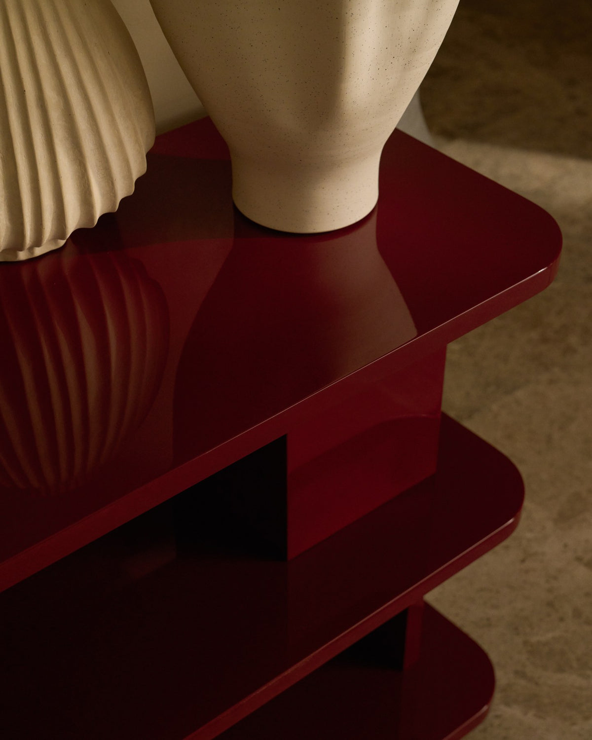 Regal Aduma aus MDF und Buchenholz mit granatroter Glanzlackierung, geschwungene Form mit offenen Fächern und verstellbaren Beinen.