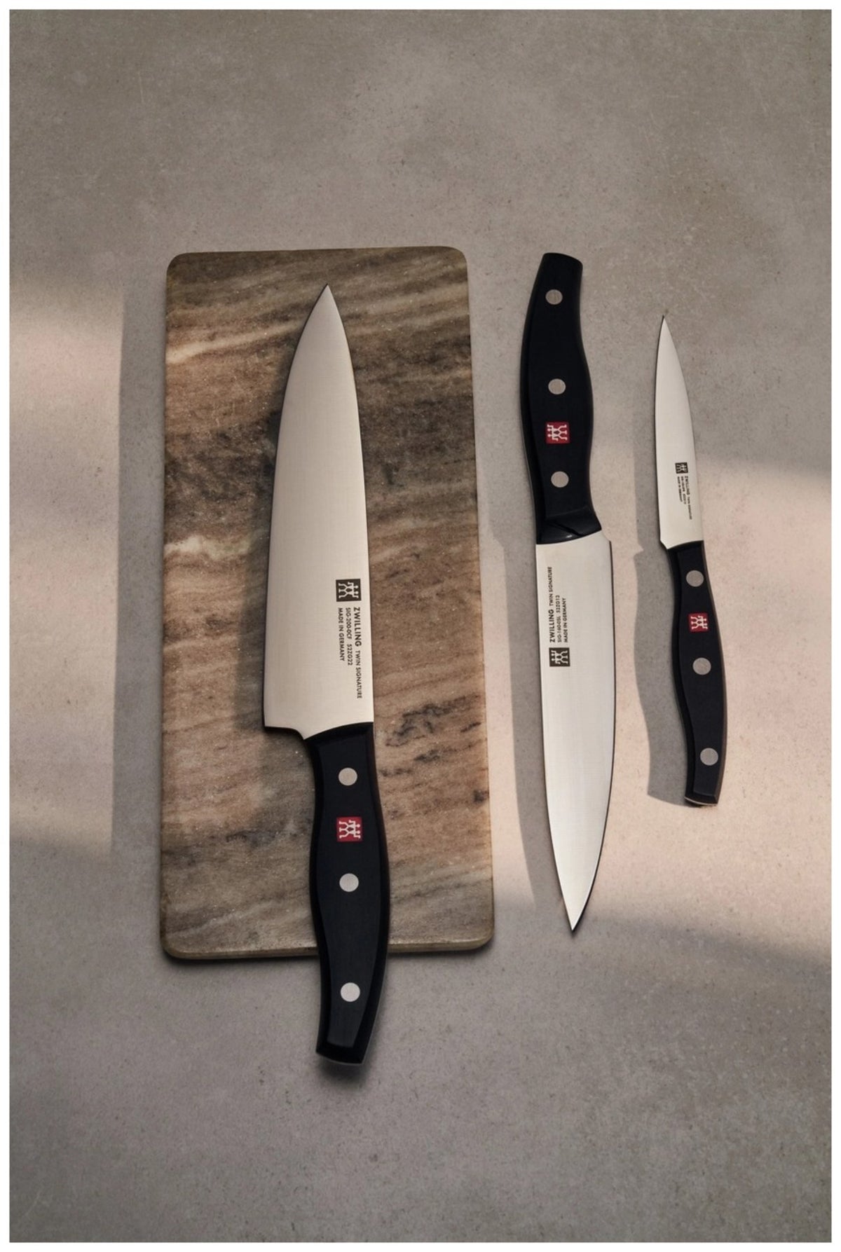 Drei Küchenmesser aus Edelstahl mit Drei-Nieten-Griff: Schälmesser, Tranchiermesser und Kochmesser der Zwilling Signature Serie, nebeneinander liegend.