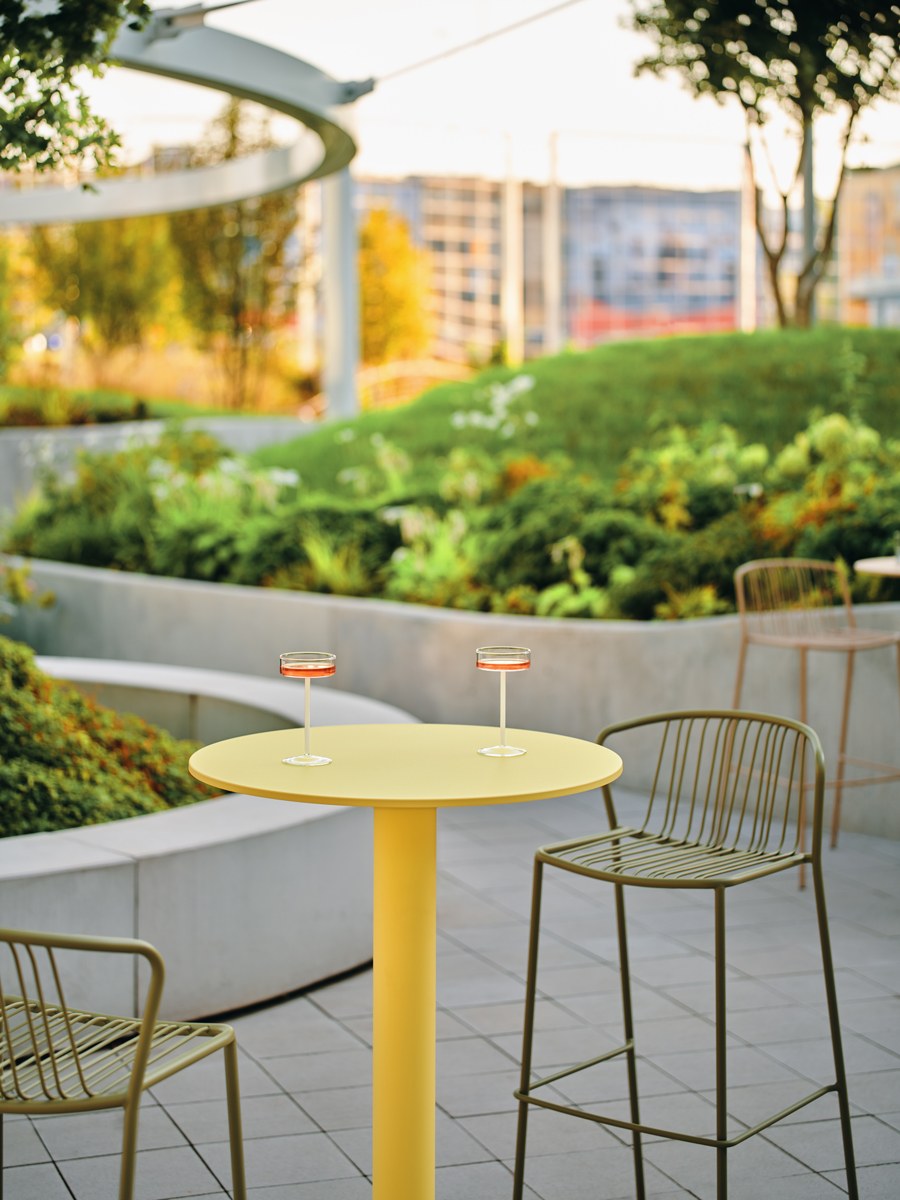 Zwei Barhocker mit durchbrochenem Sitz und Rückenlehne aus verzinktem Stahldraht, olivgrünes Gestell, schwarze Kunststofffüsse, Outdoor-Design.