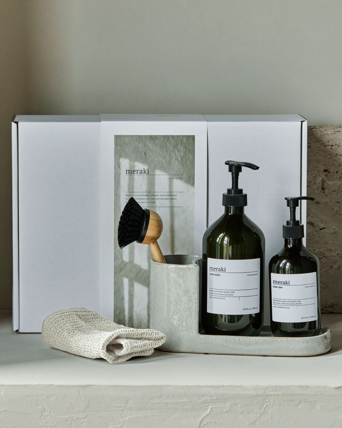 Elegantes Geschenkset von Meraki in einer grauen Box, bestehend aus einer Naturbürste, duftneutraler Handseife und Geschirrspülmittel im Waldgarten-Stil.