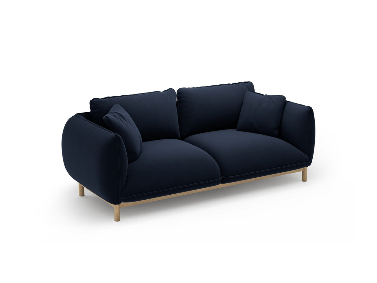 Ada 2er Sofa von Micadoni in Mandel beige mit gepolstertem Velours-Bezug, geschwungener Rückenlehne und sichtbaren Buchenholzbeinen.