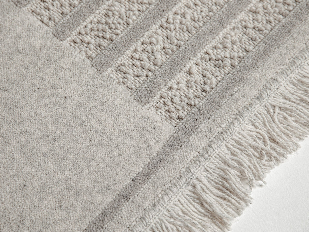 Hellgrauer Wollteppich Form von Micadoni mit reliefartigem Muster aus Cut- und Loop-Pile, Grösse 300 x 200 cm, auf hellem Boden liegend.
