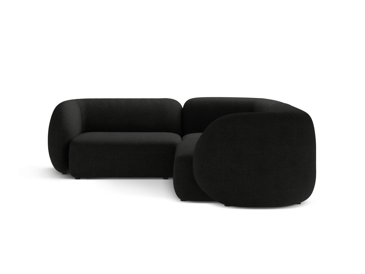 Weisses Ecksofa links Kate von Micadoni mit Bouclé-Stoff Baloo, schwarzen Kunststoffbeinen und niedriger Rückenlehne im Wohnraum.