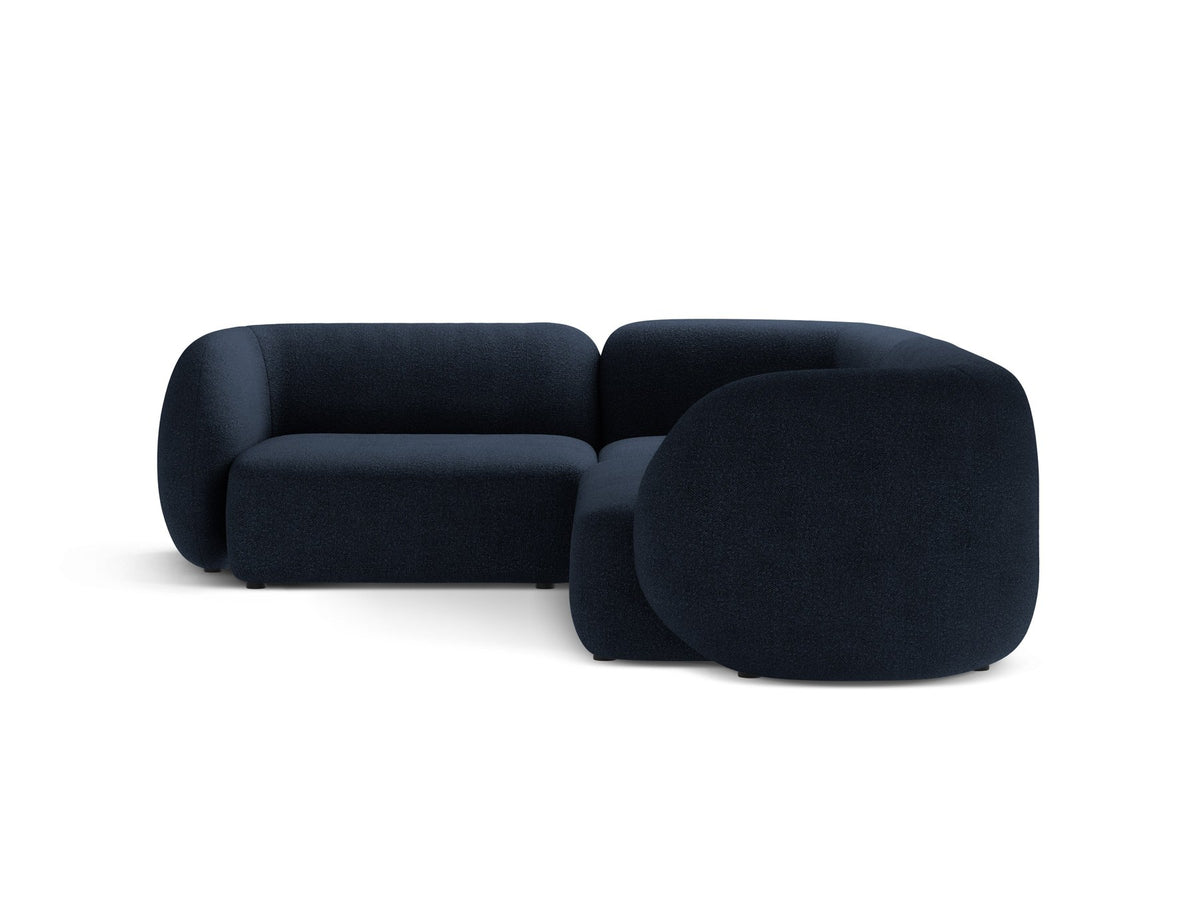 Weisses Ecksofa links Kate von Micadoni mit Bouclé-Stoff Baloo, schwarzen Kunststoffbeinen und niedriger Rückenlehne im Wohnraum.