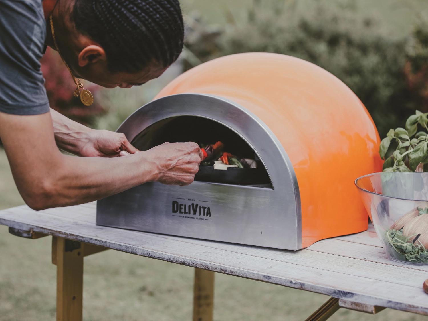 Der tragbare Delivita Holzofen in Orange ist ideal für stilvolles Outdoor-Kochen und zaubert köstliche Pizzen und mehr.