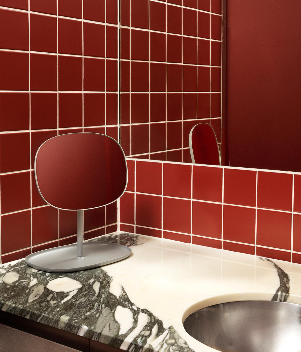 Tischspiegel Flip von Normann Copenhagen mit rundem Glasspiegel und Fuss aus beschichtetem Stahl in organischer Form, Farbe Schwarz.