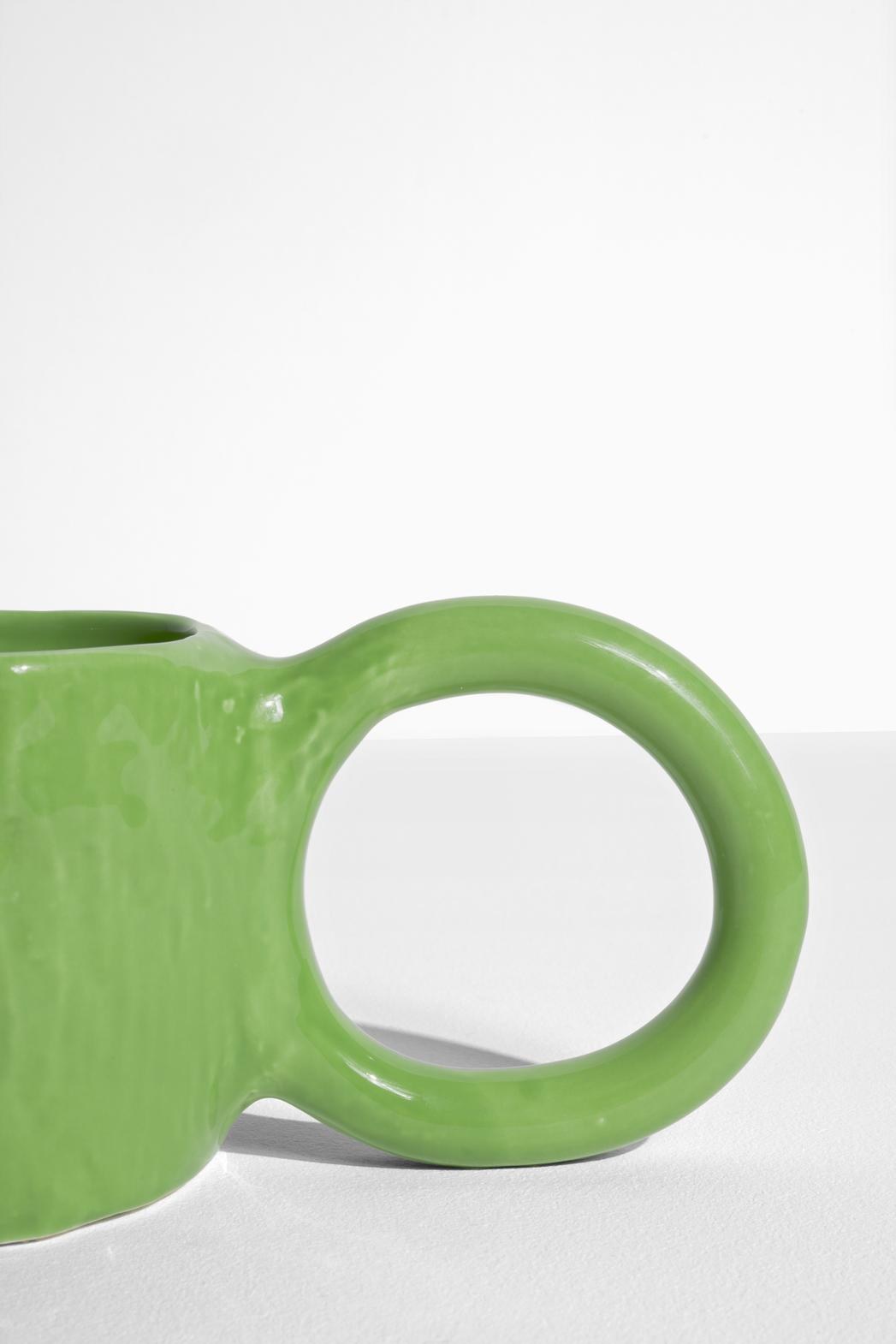 Keramiktasse Donut in Pistazie mit glasierter Oberfläche und donutförmigem Henkel, mittlere Grösse, handwerklicher Look, auf hellem Hintergrund.