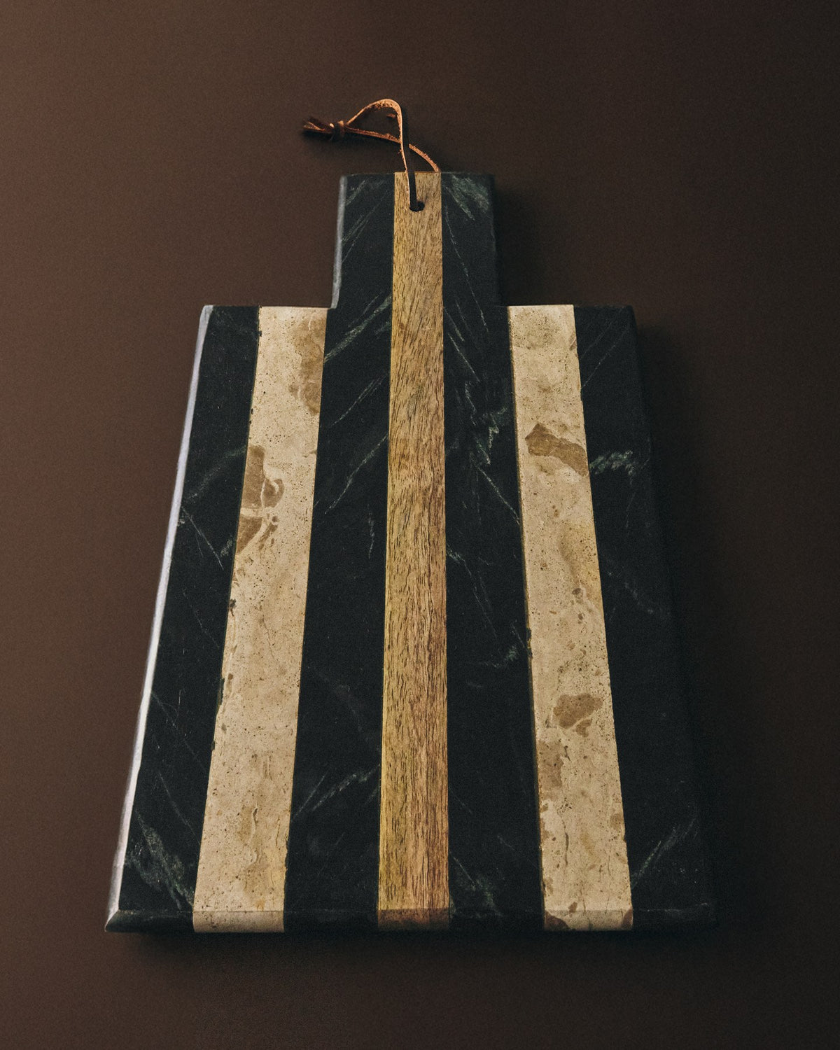 Rechteckiges Servierbrett aus Marmor in den Farben Schwarz, Braun und Beige, mit Loch am Rand, glatte Oberfläche und sichtbarer natürlicher Äderung.