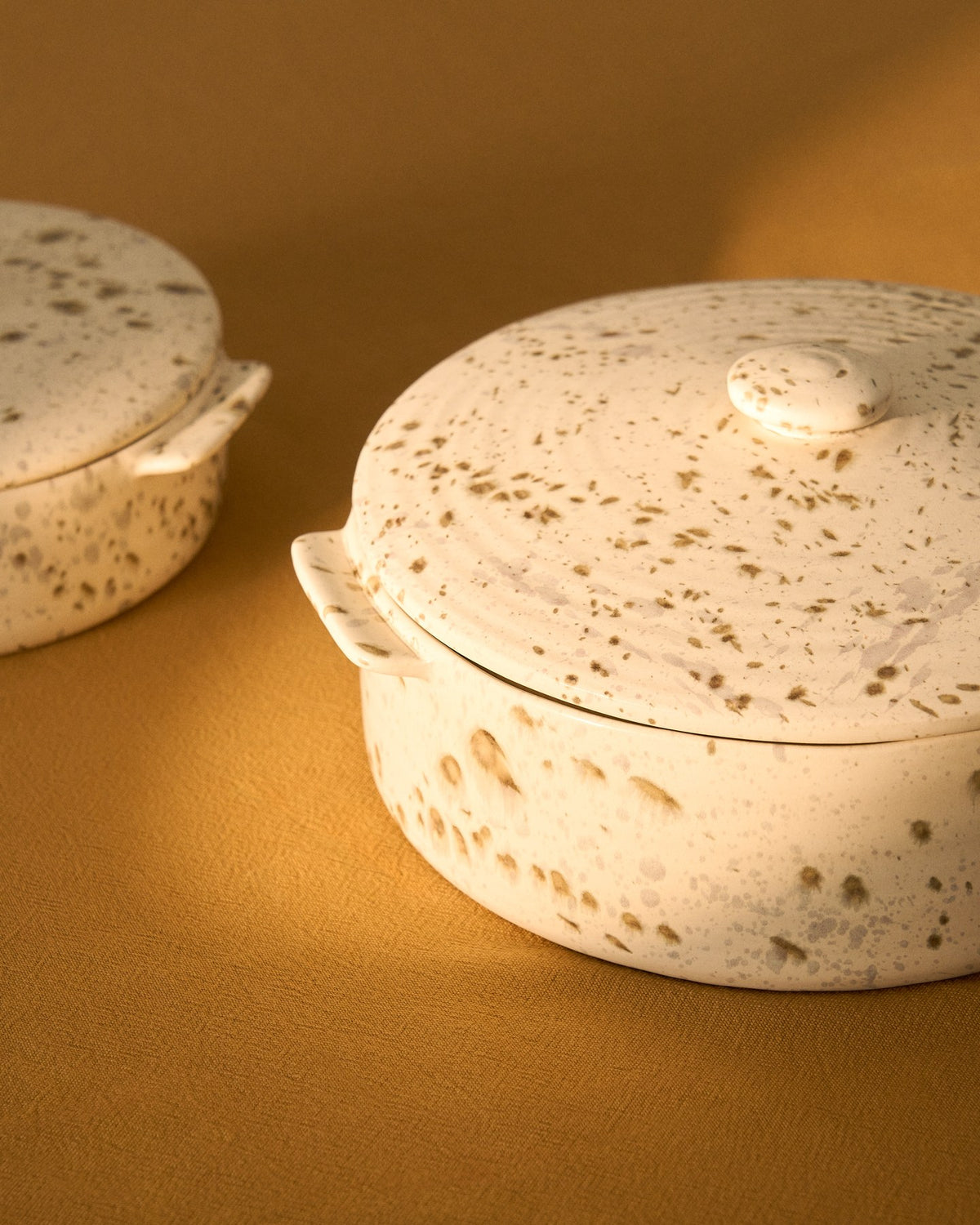 Weisse Auflaufform aus Keramik mit braunem Aufdruck und Deckel, gesprenkeltes Finish durch reaktive Glasur, rechteckige Form für den gedeckten Tisch.