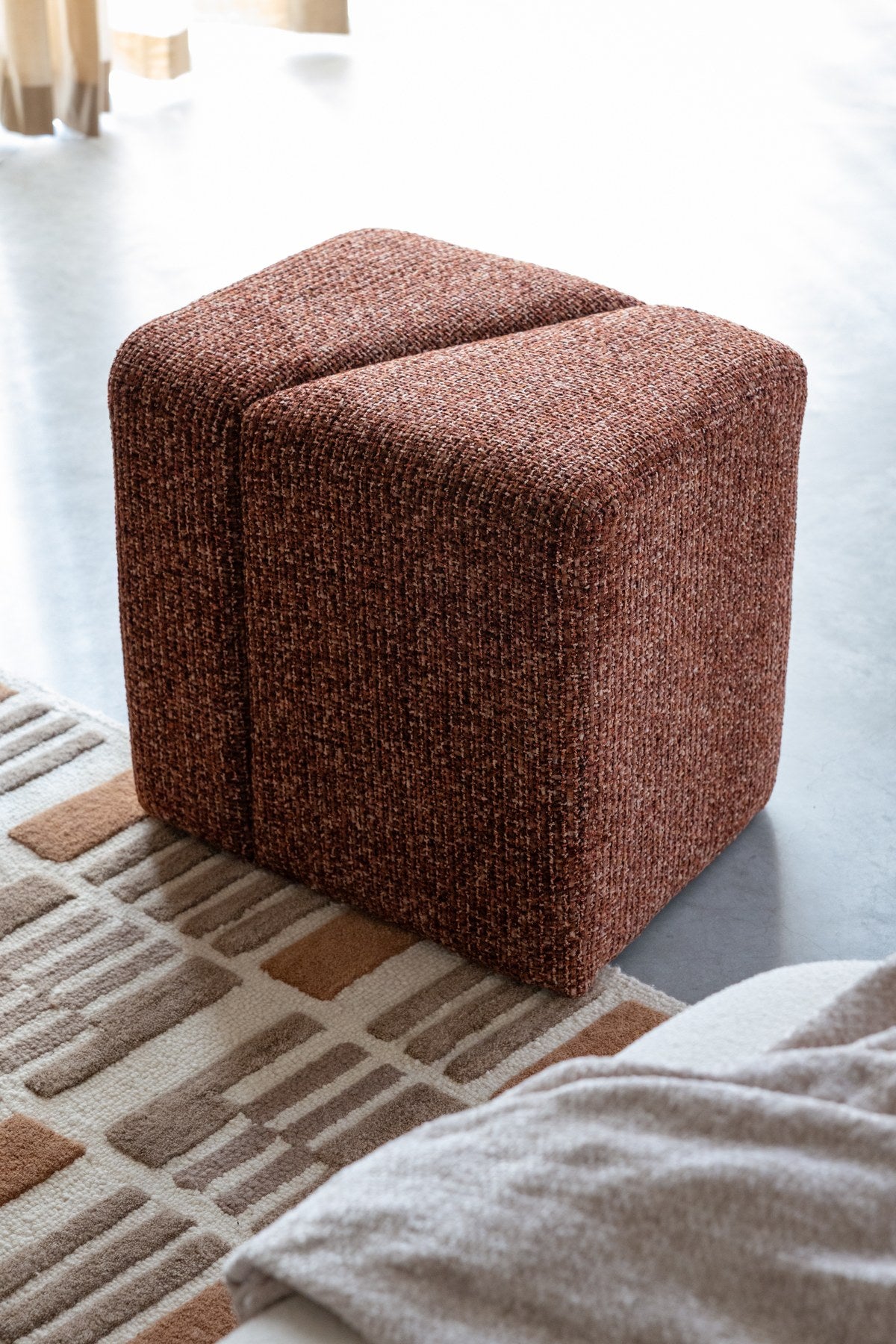 Gepolsterter Hocker Stool Dance Terracotta von White Label Living mit meliertem Terrakotta-Stoff und schrägen, versetzten Flächen.