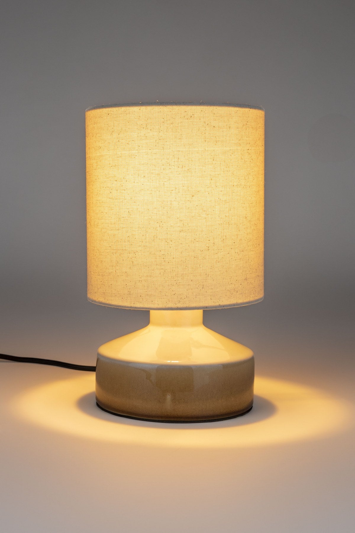Beige Tischleuchte Nook von Zuiver mit Lampenschirm aus Leinen und rundem Fuss aus glänzendem Keramik, schwarzes Textilkabel.