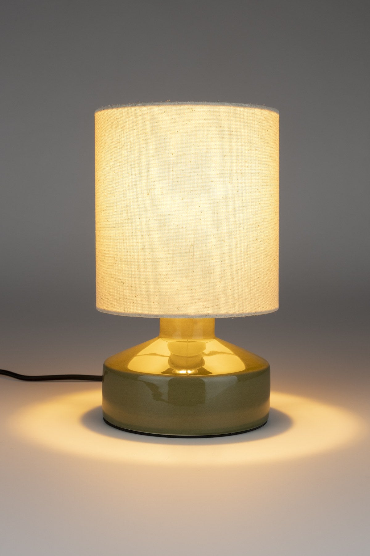 Tischlampe Nook von Zuiver in Grün: runder Lampenschirm aus Leinen auf einem Keramikfuss mit glänzender Oberfläche, Kabel aus schwarzem Textil.
