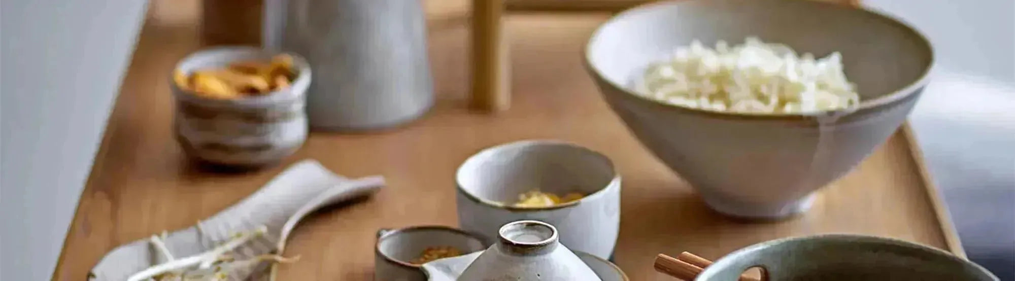 Elegantes Geschirr der Masami-Serie von Bloomingville, bestehend aus Tellern, Tassen und Schalen in sanften, erdigen Tönen mit organischen Formen und handgefertigten Details, präsentiert auf einem stilvoll gedeckten Tisch.