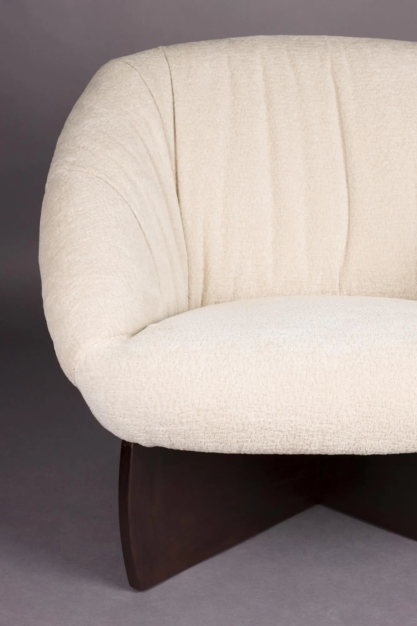 Der Emilius Loungestuhl von Dutchbone vereint luxuriösen Bouclé-Stoff mit elegantem Gummibaumholz für stilvollen Komfort.