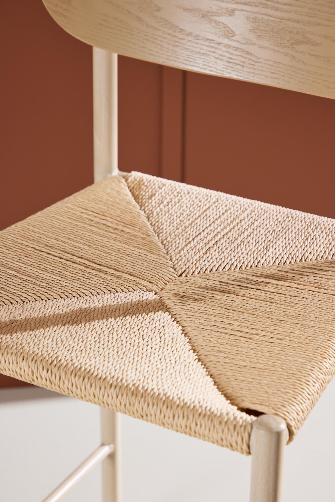 Der Polly Barstuhl vereint Rattan-Sitz und weiße Holzbeine zu einem stilvollen, platzsparenden Design für modernen Boho-Chic.