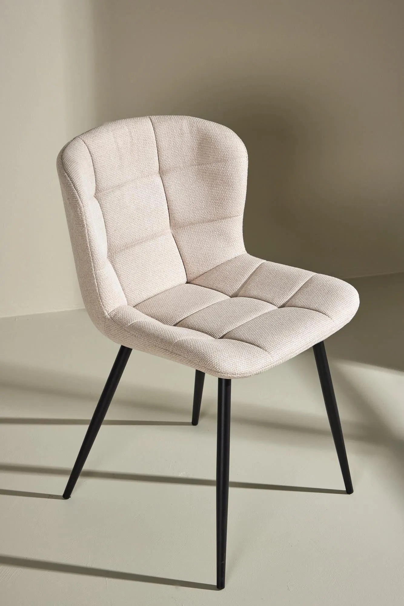 Der Lily Esszimmerstuhl vereint elegantes Design mit Komfort: Beige Polsterung, schwarze Beine, ideal für stilvolle Esszimmer.