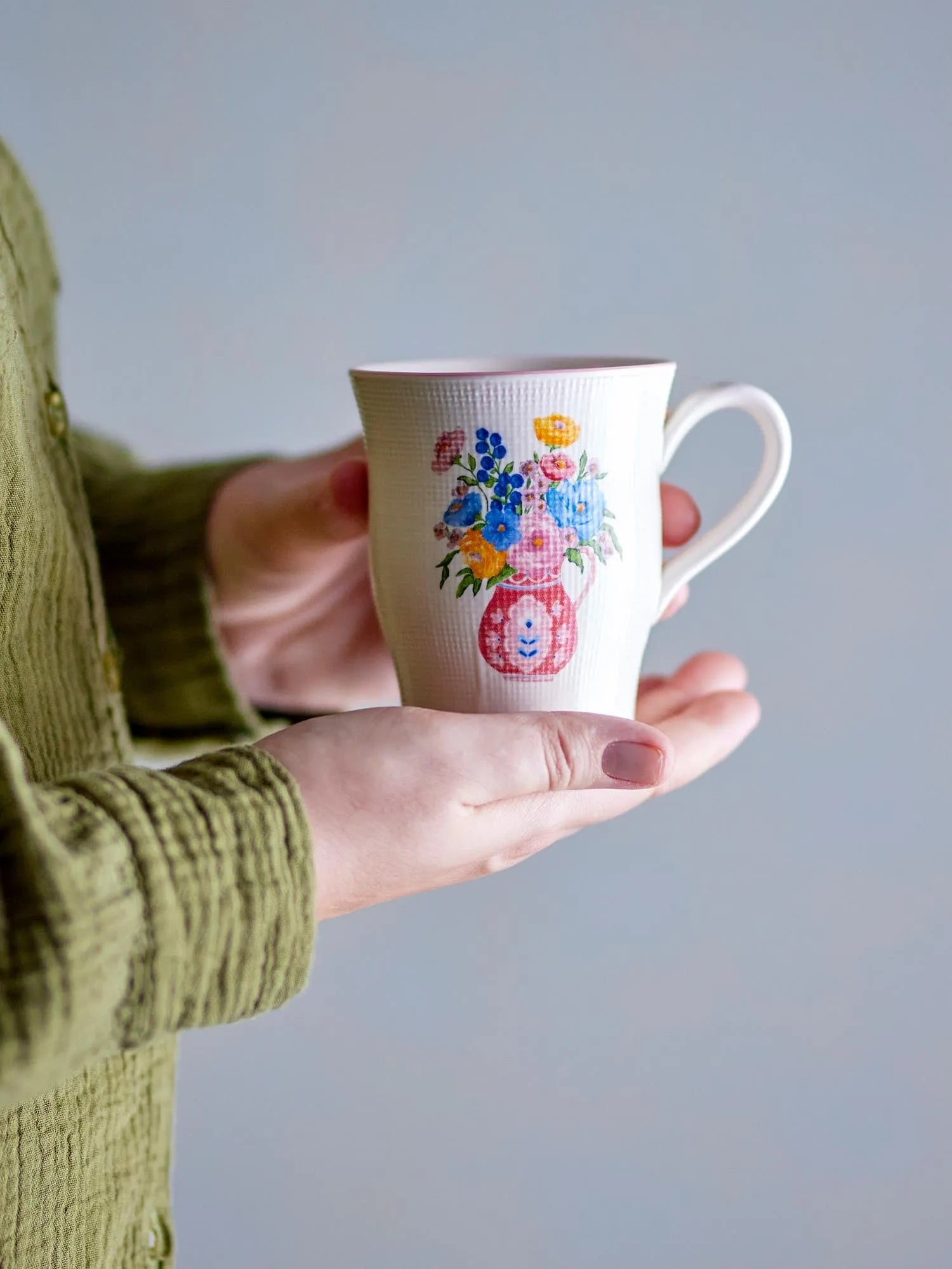 Ein stilvoller Steingutbecher mit geprägtem Blumenmotiv in lebendigen Farben und rosa Rand, ideal für Kaffee oder Tee.