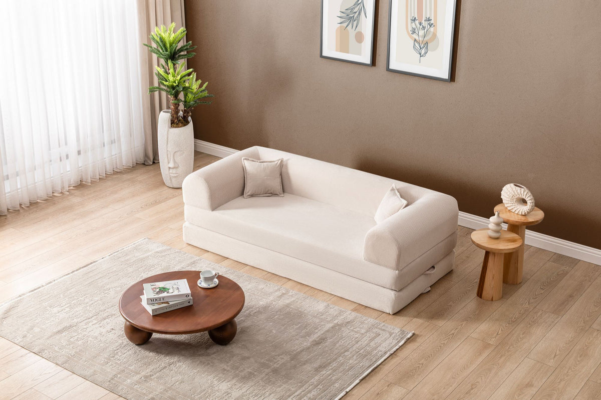 Cremefarbenes 3-Sitzer Schlafsofa Legom Eco von Hanah Home aus geripptem Cord-Plüschstoff mit zwei Kissen im Roll-Pack-Design abgebildet.