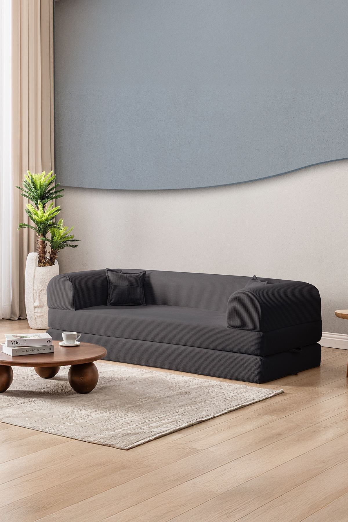 Anthrazitfarbenes 3-Sitzer Schlafsofa aus geripptem Cord-Plüschstoff mit zwei Kissen und sichtbarer rutschfester Sohle.