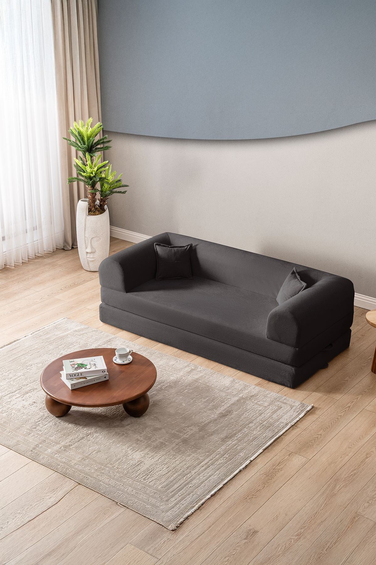 Anthrazitfarbenes 3-Sitzer Schlafsofa aus geripptem Cord-Plüschstoff mit zwei Kissen und sichtbarer rutschfester Sohle.