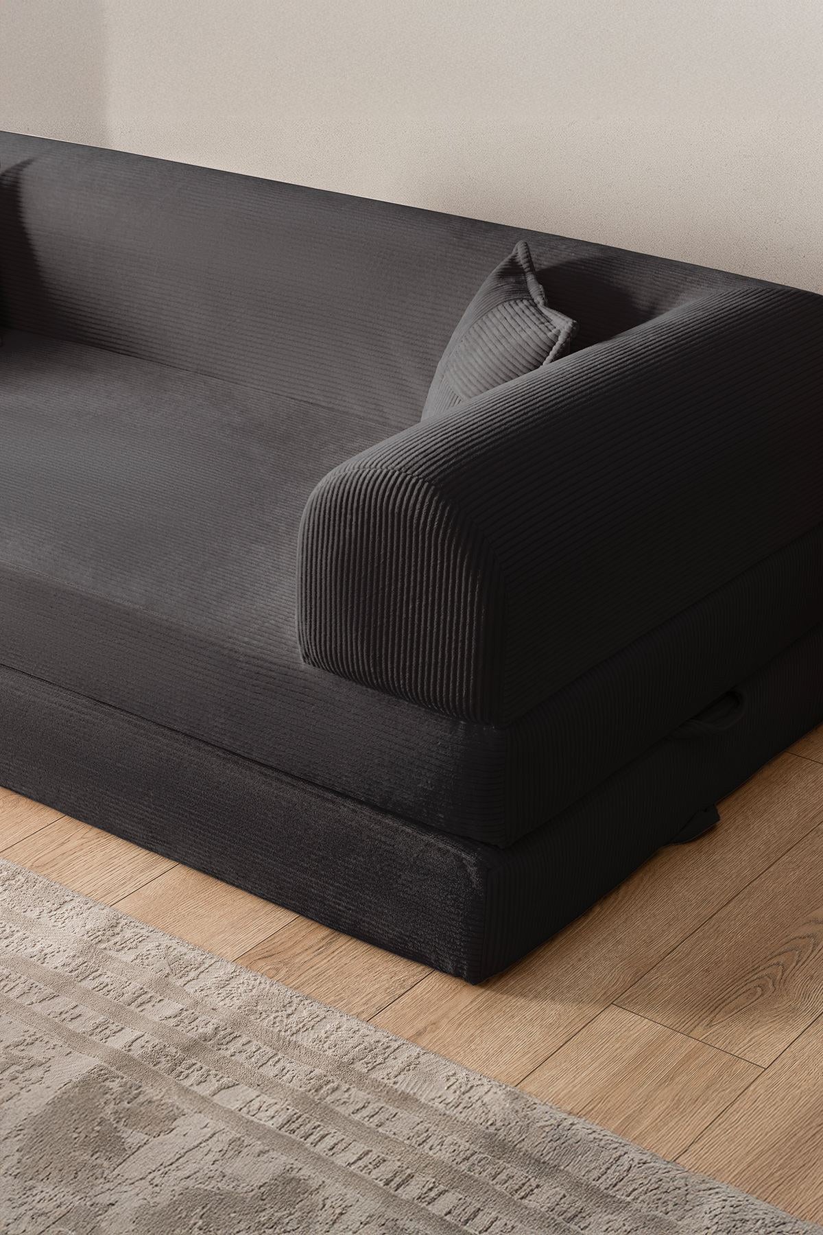 Anthrazitfarbenes 3-Sitzer Schlafsofa aus geripptem Cord-Plüschstoff mit zwei Kissen und sichtbarer rutschfester Sohle.