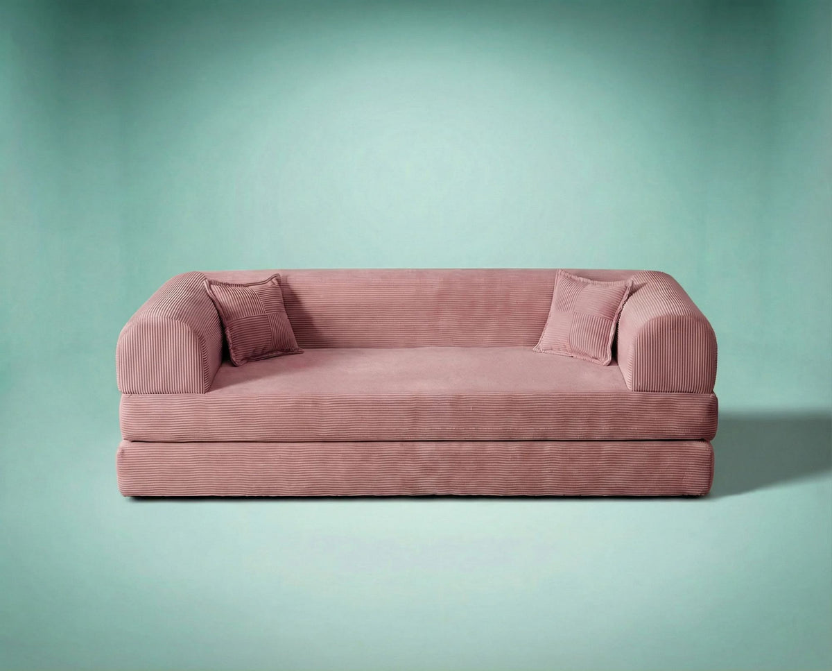 Rosafarbenes 3-Sitzer Schlafsofa aus geripptem Cord-Plüschstoff mit zwei Kissen und rutschfester Sohle, Frontalansicht auf hellem Hintergrund.