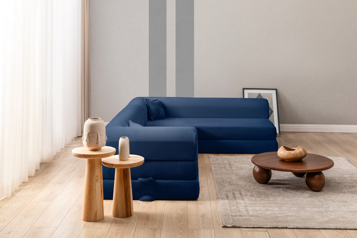 Marineblaues Ecksofa-Bett mit Cord-Plüschbezug, vier Kissen, Rückenlehne und niedriger Sitzhöhe, freistehend im Raum fotografiert.