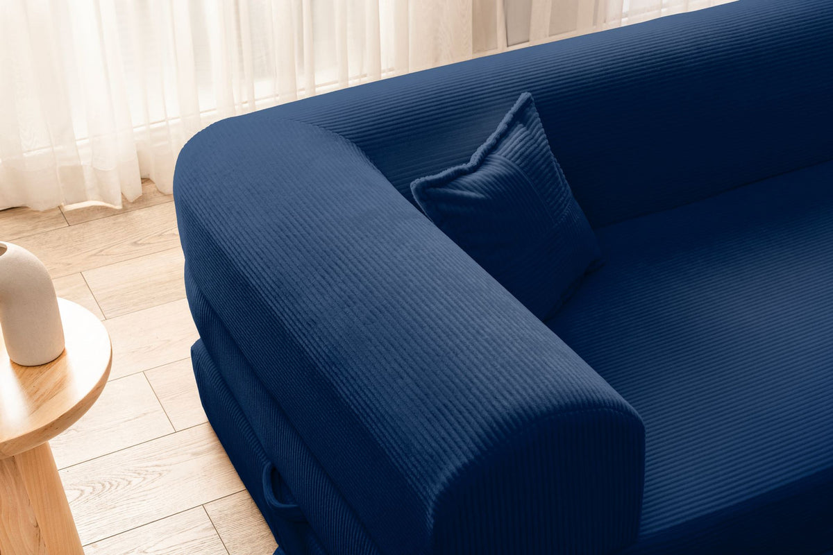 Marineblaues Ecksofa-Bett mit Cord-Plüschbezug, vier Kissen, Rückenlehne und niedriger Sitzhöhe, freistehend im Raum fotografiert.