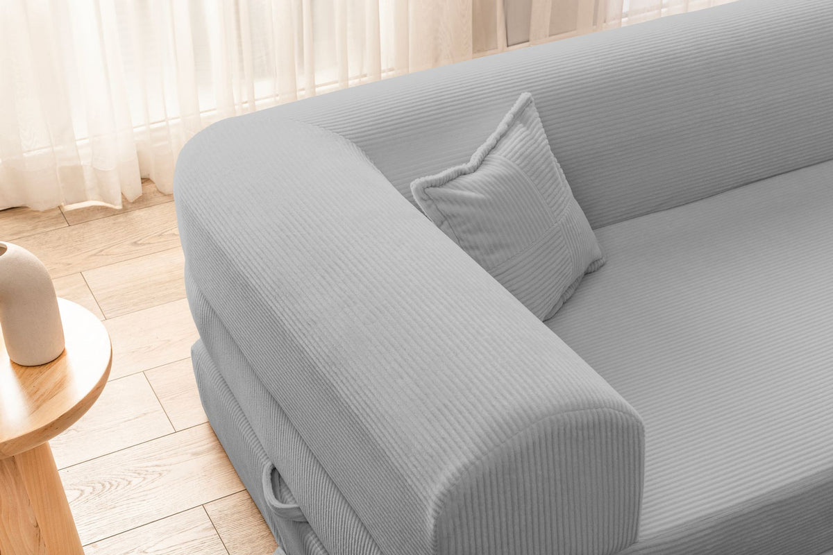 Hellgraues Ecksofa-Bett aus geripptem Cord-Plüschstoff mit niedriger Rückenlehne, vier Kissen und ausklappbarer Liegefläche.