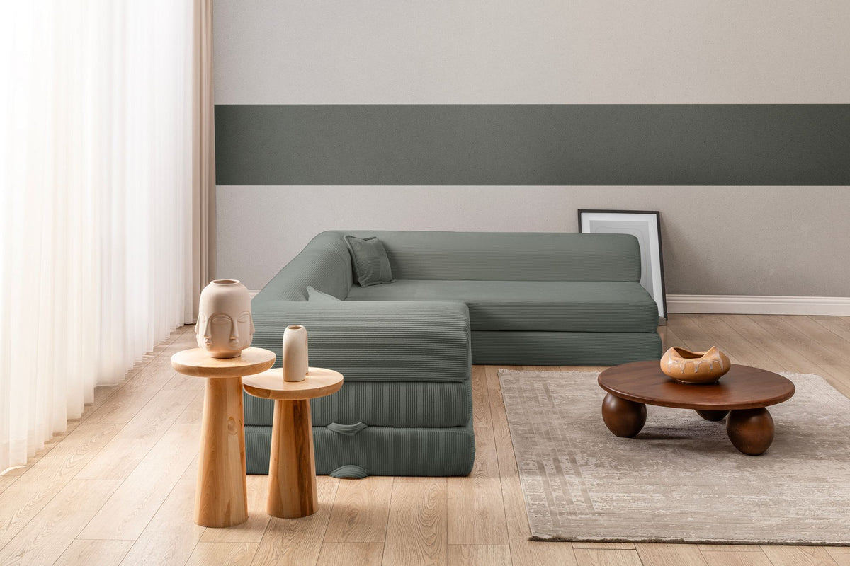 Grünes Ecksofa-Bett aus geripptem Cord-Plüschstoff mit vier Kissen, Rückenlehne und Sitzfläche aus Schaumstoff, Frontalansicht.