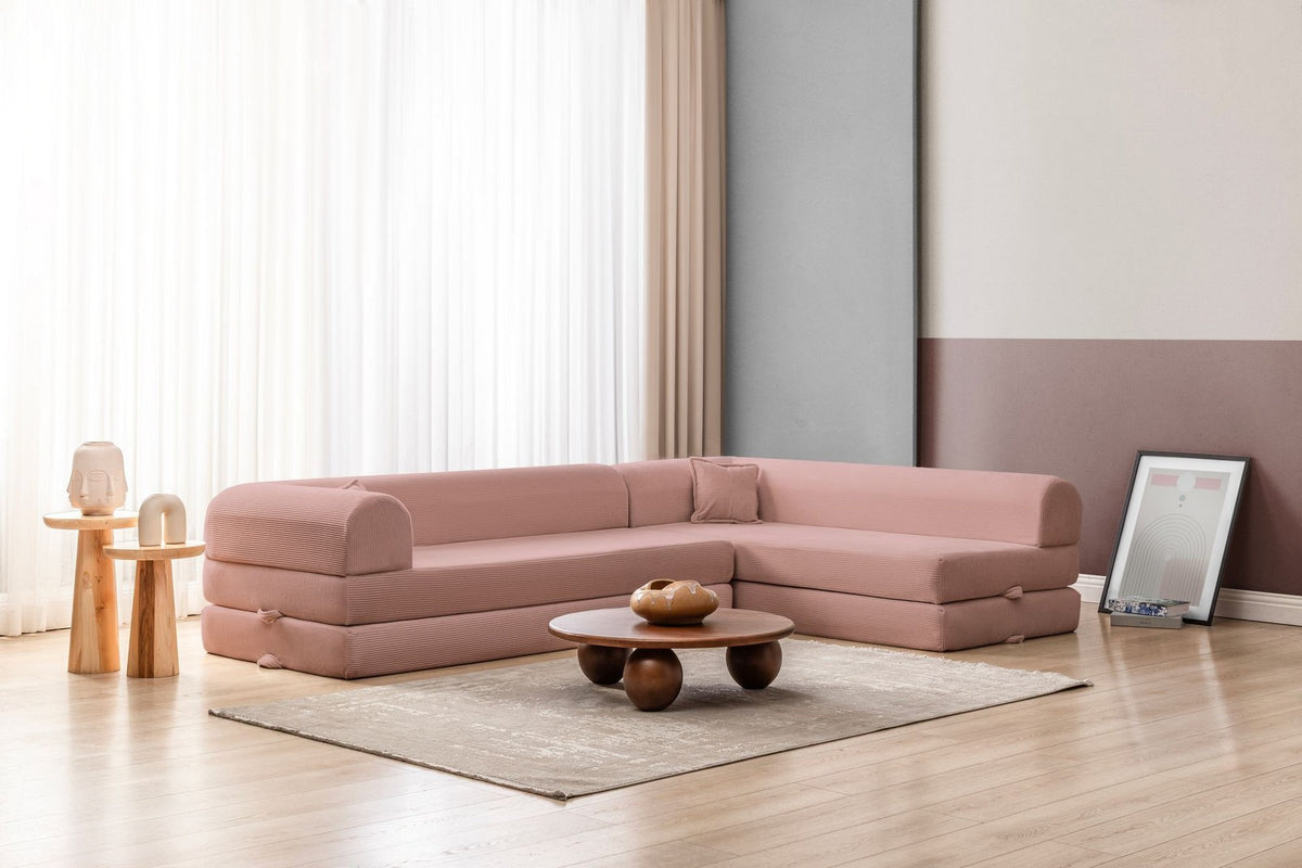 Rosa Ecksofa-Bett aus Cord-Plüschstoff mit vier Kissen, breiter Sitzfläche und niedriger Rückenlehne, als Sofa und Bett nutzbar.