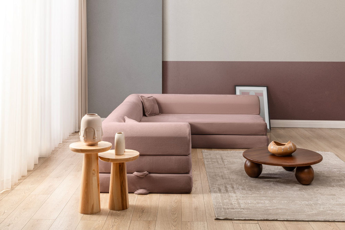 Rosa Ecksofa-Bett aus Cord-Plüschstoff mit vier Kissen, breiter Sitzfläche und niedriger Rückenlehne, als Sofa und Bett nutzbar.