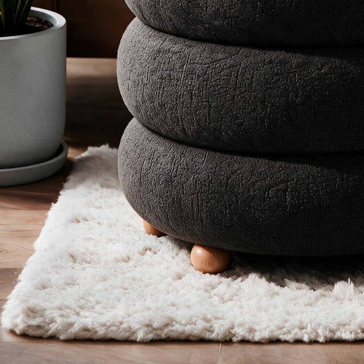Dunkelgrauer Pouf Ottavia von Hanah Home mit gestricktem Polyesterbezug, Holzkugelfüssen und verborgenem Stauraum unter der Sitzfläche.