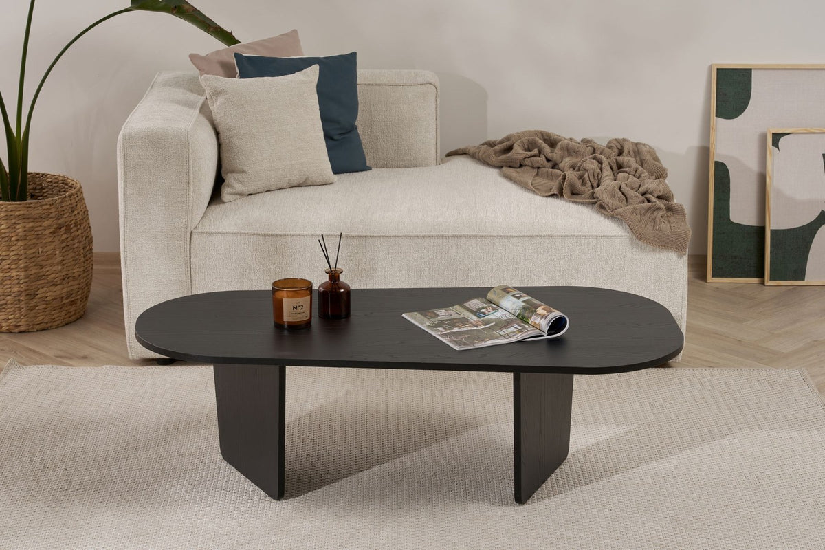 Ovaler Couchtisch aus melaminbeschichteter Spanplatte in Holz Schwarz, schlichte Form, Masse 130x65x40 cm, freistehend im Wohnraum.